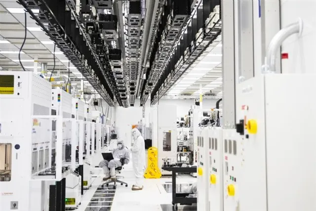 A technician working at a laptop between rows of process tools in a cleanroom aisle