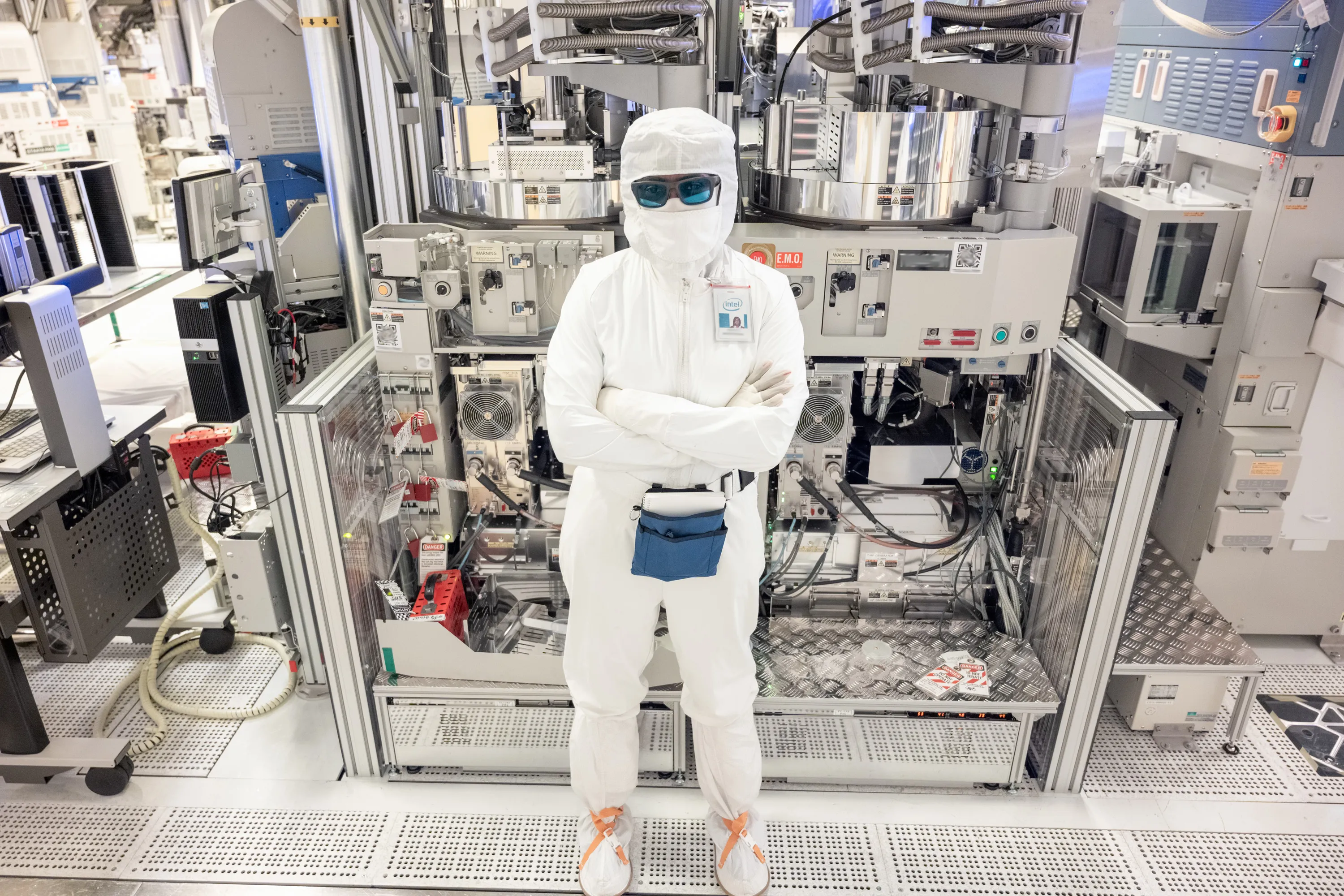 A gowned process technician standing at a process tool in a semiconductor fab