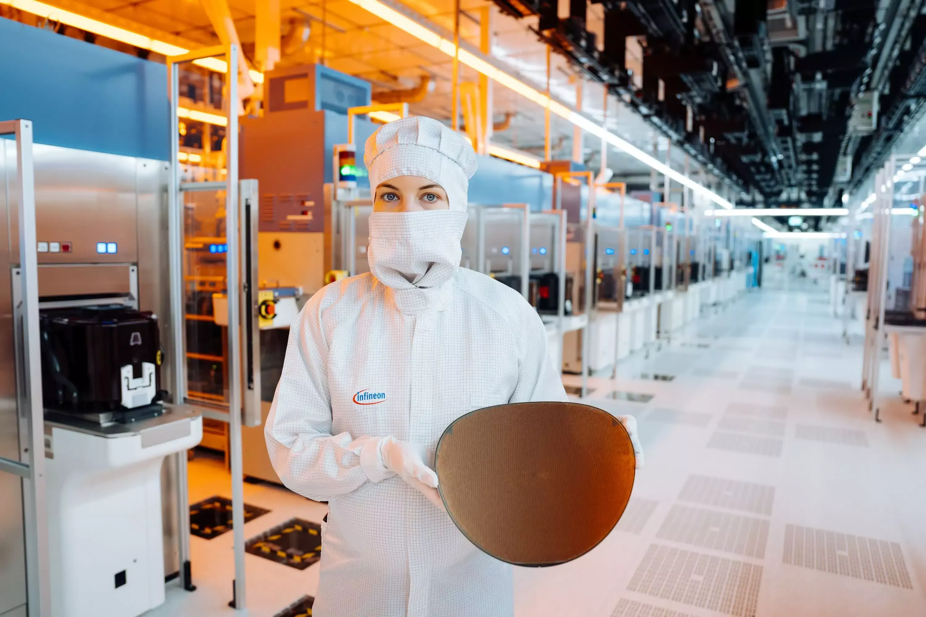 A process technician holding a patterned silicon wafer in a fab production aisle