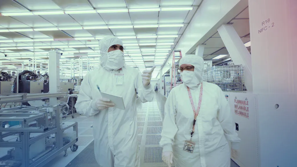 Two gowned process technicians reviewing data while walking a cleanroom aisle